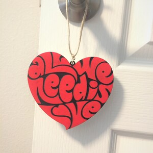 May include: Red heart-shaped wooden sign with the text "All we need is love" in black lettering.