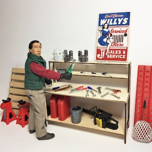 May include: A wooden workbench with two shelves, a red gas can, a chainsaw, and various tools. A man in a green vest and khaki pants stands next to the workbench. A sign above the workbench reads "Get Your Willys Serviced Here Sales & Service".