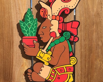 May include: A wooden figurine of a Mayan deity holding a potted plant. The figurine is painted in bright colors, including red, green, yellow, and orange. The deity is wearing a headdress with intricate details.