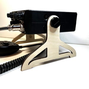 May include: A black radio transceiver mounted on a light-colored wooden stand. The stand has a unique, open design. A black microphone and coiled cord are connected to the radio. The radio has several knobs and buttons.