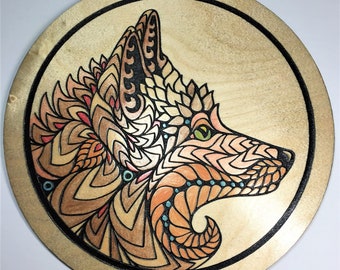 May include: A circular wooden plaque with a black border, featuring a detailed, intricate design of a wolf's head in shades of brown, orange, and teal.