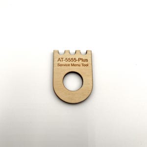 May include: A wooden tool with a small hole and a notched top. The tool is labeled "AT-5555-Plus Service Menu Tool".