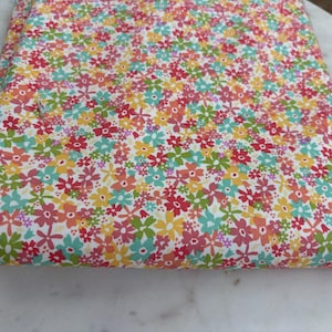 May include: A folded piece of fabric featuring a dense, repeating pattern of small flowers in shades of red, pink, yellow, and light blue on a white background. The floral print covers the entire visible surface of the textile.