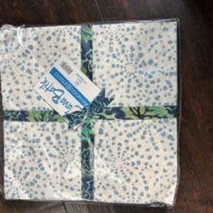 May include: A package of fabric squares, featuring a white background with blue and gray dot patterns. The squares are tied with a patterned ribbon and a tag that reads "Java Batik". The fabric is packaged in clear plastic.