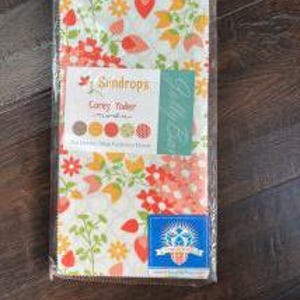 May include: A fabric bundle featuring a floral pattern with red strawberries, yellow tulips, and green leaves on a white background. The bundle is wrapped in clear plastic and includes a label that reads "Sundrops Corey Yoder."