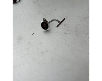 Pin de corbata vintage con inicial F en esmalte negro tono plata y cadena en forma de T.