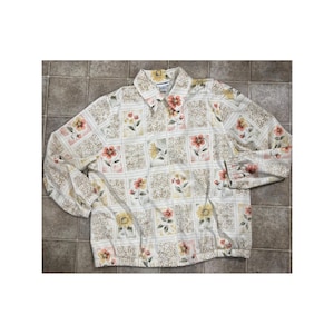 May include: A long-sleeved button-down shirt with a floral pattern. The shirt features a cream-colored background with a repeating pattern of squares, each containing a different flower design in shades of yellow, orange, and pink.