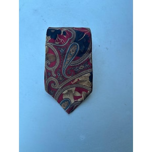 Puede incluir: Una corbata con un fondo rojo vibrante y un complejo patrón de cachemira multicolor. El diseño incorpora intrincados remolinos, motivos florales y formas de lágrima en tonos azul marino, dorado y crema, creando una textura visual densa y ornamentada en toda la superficie de la tela.