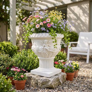 May include: A large white urn planter filled with colorful flowers, including pink, yellow, and purple blooms. The planter features cherub relief details and sits on a stone base. Small terracotta pots with flowers are in the foreground.