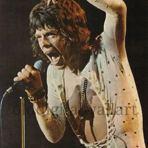 Puede incluir: Fotografía vintage de un artista en el escenario, cantando en un micrófono. El artista lleva una camisa blanca con pequeños puntos negros y una parte delantera con cordones, y pantalones rojos. El artista se está agarrando el pelo.