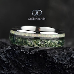 May include: A silver-toned ring with a wide band. The ring features a central band of green and white speckled material, framed by a polished silver edge. The text "Stellar Bands" is visible in the background.