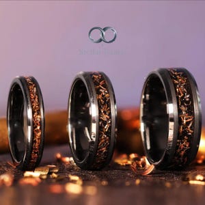 May include: Three black rings with a copper-colored inlay. The rings have a polished finish and a band of copper-colored material in the center. The rings are displayed on a dark surface with the text "Stellar Bands".