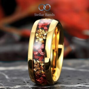 May include: A gold-colored ring with a central band filled with red and gold-colored fragments. The ring has a polished, reflective surface. The brand name "Stellar Bands" is visible in the background.