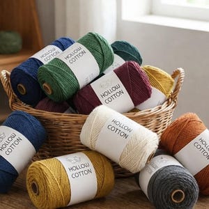 May include: A collection of colorful spools of "Hollow Cotton" yarn in a wicker basket and scattered around it. The yarn colors include navy blue, green, burgundy, yellow, cream, and rust. Each spool has a white label with the text "Hollow Cotton".