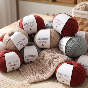 Puede incluir: Una colección de ovillos de lana merino en varios colores, incluyendo rojo, beige y gris. Cada ovillo tiene una etiqueta blanca con el texto "MERINO WOOL". También se ve una pequeña muestra tejida.