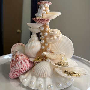 May include: A white ceramic mug with a black handle and the text "But First, Coffee" in a bold, black font. The mug is set against a blurred background, suggesting a cozy setting.