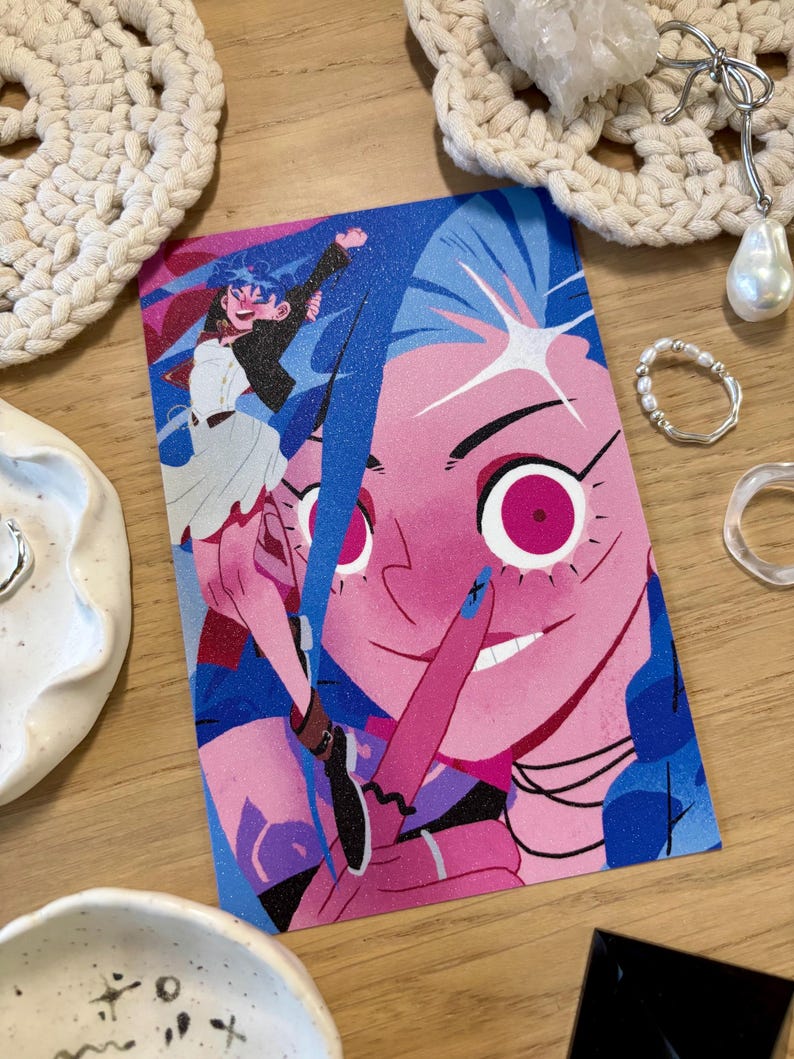 Puede incluir: Una colorida impresi&oacute;n art&iacute;stica que presenta una ilustraci&oacute;n estilizada de un personaje con piel rosa y cabello azul. La obra de arte presenta un gesto de dedo en los labios y una paleta de colores vibrantes.