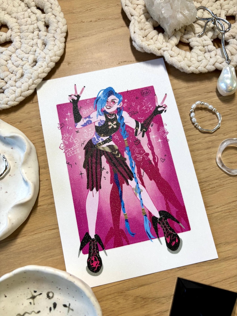 Puede incluir: Ilustraci&oacute;n vibrante de un personaje con cabello azul, sobre un fondo rosa. El personaje lleva un atuendo negro y tacones altos. La obra de arte est&aacute; en una tarjeta blanca, rodeada de objetos decorativos.
