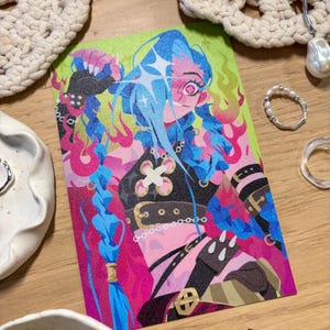 Puede incluir: Una colorida impresi&oacute;n art&iacute;stica que presenta un personaje estilizado con cabello azul en una pose din&aacute;mica. La obra de arte muestra vibrantes tonos rosa, verde y rojo, con detalles como llamas y un dise&ntilde;o en forma de cruz. El personaje lleva una parte superior negra con detalles dorados.