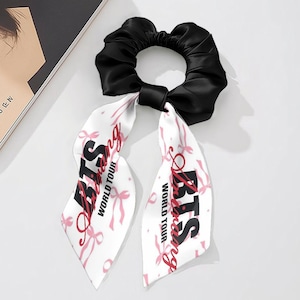 May include: Black satin scrunchie with white ribbon tails. The ribbons feature pink bows and the text "BTS Loving World Tour" in black and red. A stylish hair accessory.