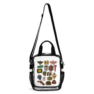 May include: A clear plastic crossbody bag with black trim, two top handles, and an adjustable shoulder strap. The front features various colorful patches, including a television, scissors, a pistol, and signs with text like 23 and 13 North.