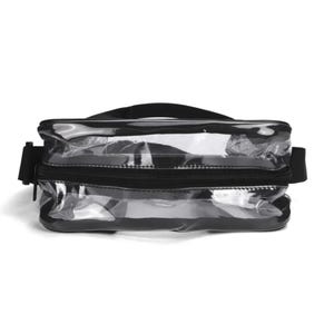May include: A clear rectangular waist bag featuring black trim and a black zipper closure. The bag includes an adjustable black strap attached to the sides, providing a transparent view of the interior compartment through the plastic material.