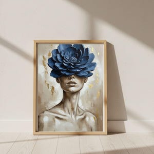 May include: A framed art print featuring a woman with a large, blue flower covering her eyes. The artwork has a neutral background with gold accents. The woman's skin tone is light, and the flower is a deep shade of blue.