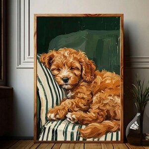 Puede incluir: Una impresión artística enmarcada de un cachorro durmiendo con pelo rizado de color marrón rojizo. El perro descansa sobre un cojín a rayas y una silla verde. La obra de arte está enmarcada en un tono de madera natural, creando una escena acogedora.