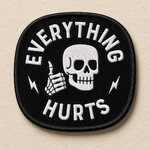 May include: A black embroidered patch with a white border, featuring a white skull giving a thumbs up. The text "EVERYTHING" is arched above the skull, and "HURTS" is below. Two small white lightning bolt icons flank the skull on each side.