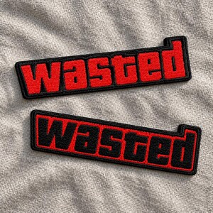 May include: Two rectangular embroidered patches featuring the word "wasted" in a bold, block-style font. The top patch has red lettering on a black background, while the bottom patch features black lettering on a red background with a black border.