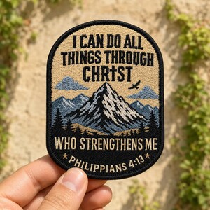 May include: An oval embroidered patch featuring a mountain landscape with blue and white peaks, dark green pine trees, and a small bird. The text reads I CAN DO ALL THINGS THROUGH CHRIST WHO STRENGTHENS ME and PHILIPPIANS 4:13 in black lettering.