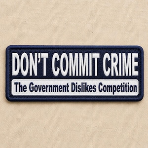 May include: A rectangular embroidered patch with a dark blue background and a thick dark blue border. The text DON'T COMMIT CRIME is stitched in white capital letters. Below, a white horizontal bar contains the text The Government Dislikes Competition.