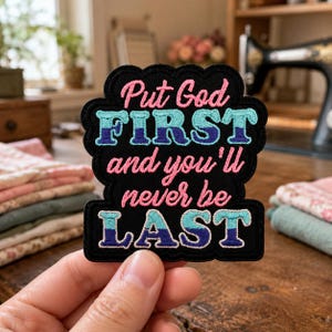 May include: A black embroidered patch with a scalloped edge featuring the pink text Put God FIRST and you'll never be LAST, with the words FIRST and LAST rendered in a two-tone teal and dark blue gradient thread against the black background.