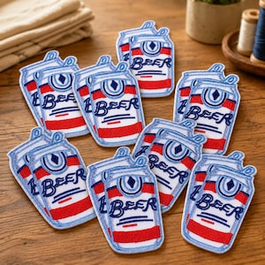 May include: A collection of embroidered patches shaped like beer cans. Each patch features a white background with red horizontal stripes, blue outlines, and the word BEER stitched in blue lettering above a blue diamond icon and horizontal lines.