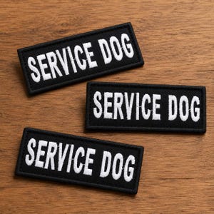 May include: Three rectangular black patches with white embroidered text that reads SERVICE DOG in capital letters. Each patch features a clean, stitched border and a bold, sans-serif font, designed for clear identification and high visibility.
