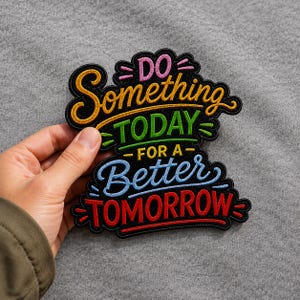 May include: A black embroidered patch featuring the colorful text DO Something TODAY FOR A Better TOMORROW. The word DO is pink, Something is yellow, TODAY is green, FOR A is yellow, Better is light blue, and TOMORROW is red, all with black borders.