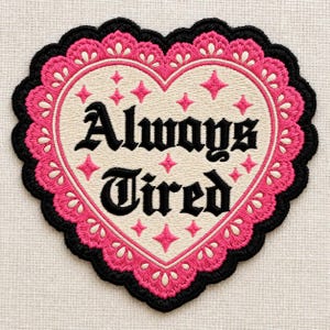 May include: A heart-shaped embroidered patch with a cream-colored center featuring the black text "Always Tired" surrounded by small pink four-pointed stars. The border consists of a scalloped pink lace-like design edged in black thread.