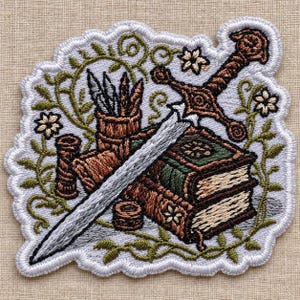 May include: An embroidered patch featuring a sword resting across two stacked books, a quill holder with three quills, and two small spools of thread. The design is surrounded by green vines and small white flowers, all outlined in white thread.