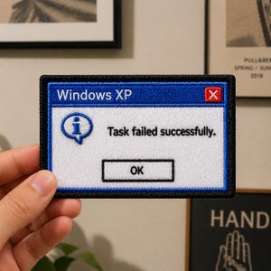May include: Embroidered patch featuring a blue and white Windows XP error message. The text reads "Windows XP", "Task failed successfully.", and "OK". The patch has a black border and is rectangular in shape.