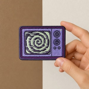 May include: Embroidered patch featuring a purple retro television with a green and white spiral design on the screen. The patch has a dark purple border and includes details like knobs and a speaker.