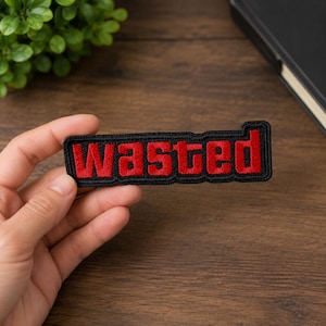 May include: A rectangular embroidered patch featuring the word WASTED in bold red capital letters with a thick black border. The lettering is stylized with a blocky font, and the entire patch has a textured, stitched finish throughout.