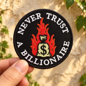 May include: A circular embroidered patch with a black background and a white border. The text NEVER TRUST A BILLIONAIRE is stitched in white around the edge. In the center, a light yellow money bag with a dollar sign is surrounded by red flames.