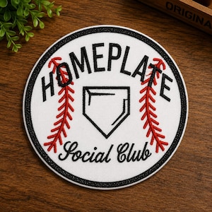 May include: A circular embroidered patch with a white background and a black border. It features the black text HOMEPLATE at the top and Social Club at the bottom, with a central black home plate icon flanked by two red baseball-style stitch patterns.