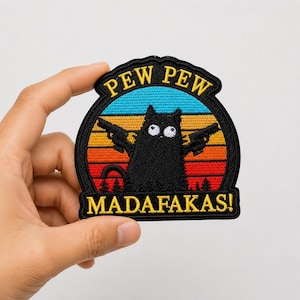 May include: A circular embroidered patch featuring a black cat with wide eyes holding two pistols. The background shows a sunset with horizontal stripes of blue, orange, and red. The text PEW PEW is at the top and MADAFAKAS! is at the bottom.