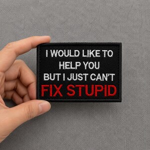 May include: A rectangular black embroidered patch with a stitched border. The text reads I WOULD LIKE TO HELP YOU BUT I JUST CAN'T in white capital letters, with the word FIX STUPID embroidered in bold red capital letters underneath.