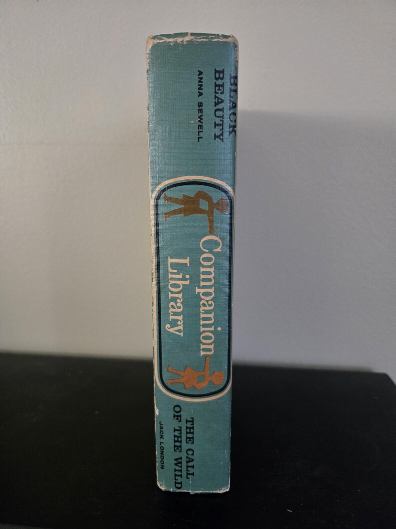 May include: A vintage book spine with the titles "Black Beauty" by Anna Sewell and "The Call of the Wild" by Jack London. The spine is teal with a gold and brown illustration and text for "Companion Library".