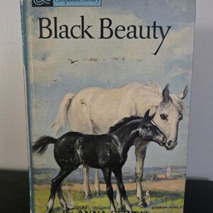 May include: Vintage hardcover book titled "Black Beauty" by Anna Sewell. The cover features a painting of a black foal and a white horse in a field. The book is part of the Companion Library series.
