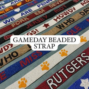 May include: A collection of beaded straps in various colors, featuring team names and phrases like "GO", "HOKIES", and "RUTGERS". The straps are adorned with paw prints and stars, perfect for game day.