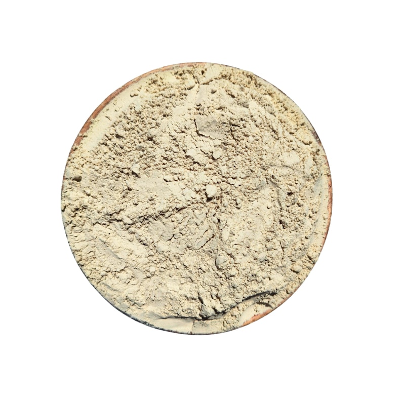 May include: A top-down view of a round, light brown bowl filled with a beige powder. The bowl has a darker brown rim. The powder has a textured, granular appearance, suggesting a fine, natural substance.