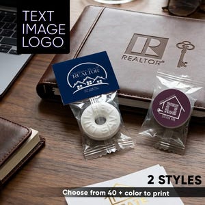 May include: Two individually wrapped promotional items for real estate professionals. One is a white ring-shaped candy with a dark blue header card featuring a house logo and text. The other is a round sticker in a clear bag with a house-shaped QR code.